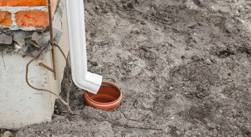Biała rura odprowadza wodę z rynien do brązowej studzienki.