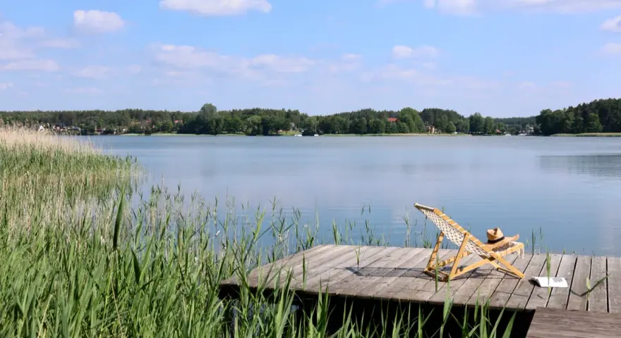 Spokojne kaszubskie jeziora, drewniany pomost z leżakiem i książką, otoczone trzcinami i lasem.