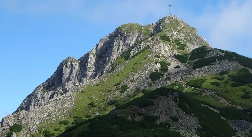 Szczyt Giewontu z krzyżem, zielone zbocza, kamienie i ścieżka. Wjazd na Giewont jest darmowy, ale wymaga wysiłku.