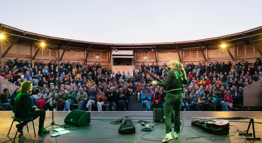 Konzert auf dem Tempelhofer Feld: Eine Musikerin spielt Gitarre vor einem begeisterten Publikum in einem hölzernen Amphitheater. Ein wahrer luftschloss tempelhofer feld Traum.