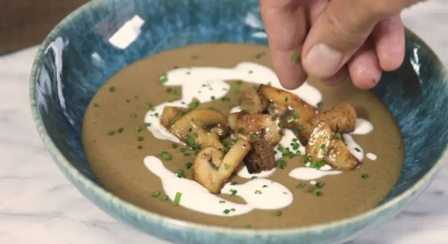 Crema de champiñones servida en un cuenco azul, decorada con champiñones salteados, picatostes y un chorrito de nata.