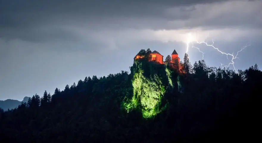 Zamek Poenari, oświetlony na czerwono, góruje nad skalistym zboczem podczas burzy z piorunami.