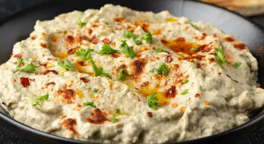Kremowa pasta z bakłażana, doprawiona papryką i posypana natką pietruszki, w czarnej misce. Idealna do pieczywa.