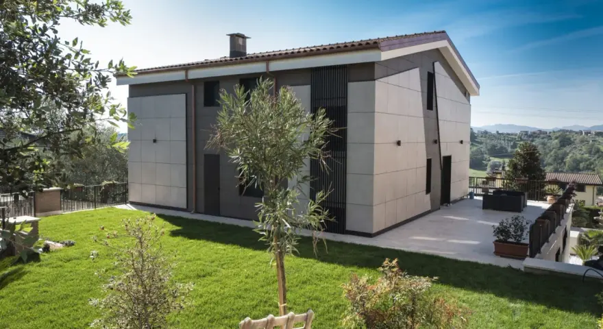 Esterno di case moderne con facciata in pannelli chiari e scuri, giardino curato e vista panoramica.