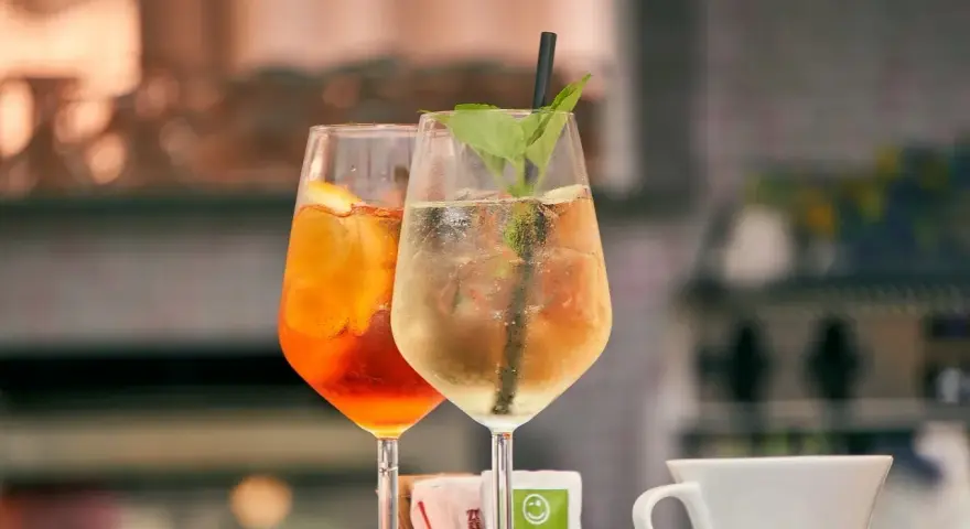 Dwa drinki w kieliszkach: pomarańczowy Aperol i jasny, z miętą. Aperol kontra Campari – wybór należy do Ciebie!