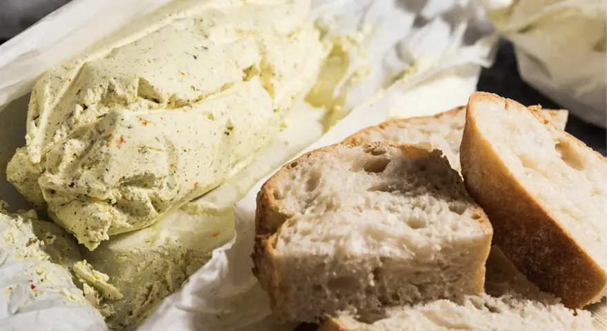 Ein Laib Kräuterbutter, wie Cafe de Paris Butter, liegt neben frisch geschnittenem Baguette.