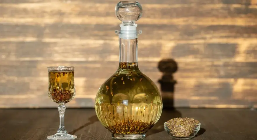 Wódka z pieprzem przepis: nalewka w karafce i kieliszku, obok miseczka z ziarnami pieprzu.
