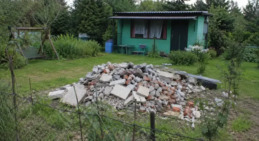 Kupa gruzu na działce ROD. Czy komornik może zająć działkę ROD? W tle zielona altanka, huśtawka i drzewa.
