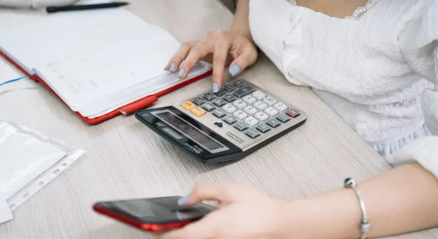 Kobieta liczy na kalkulatorze, przygotowując się do rozliczenia podatkowego w Holandii. Obok leży telefon i notatnik.