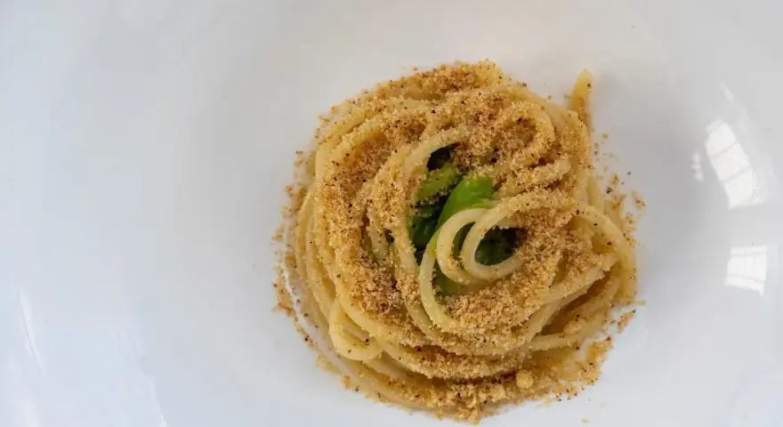 Spaghetti conditi con aglio, olio e peperoncino, cosparsi di pangrattato croccante e qualche foglia verde.