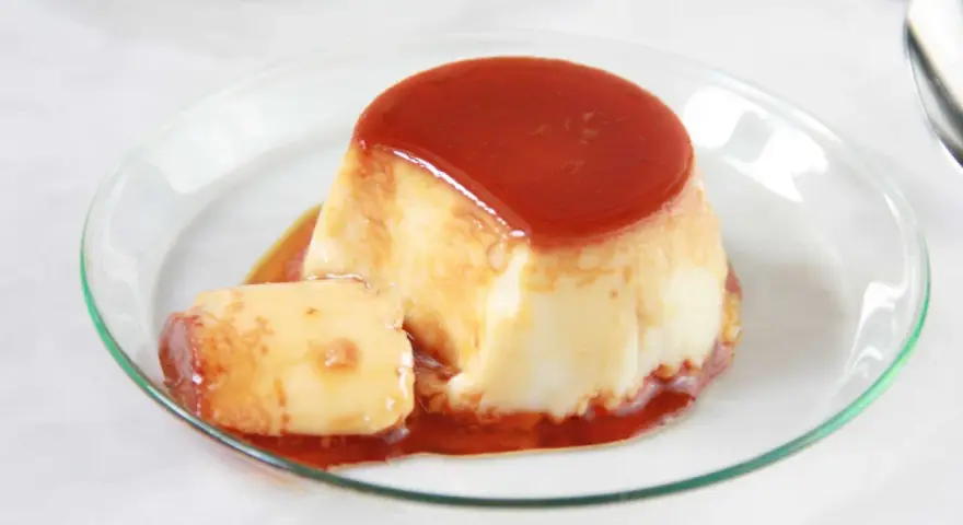 Delicioso flan de huevo en flanera con tapa, bañado en caramelo líquido y servido en un plato de cristal.