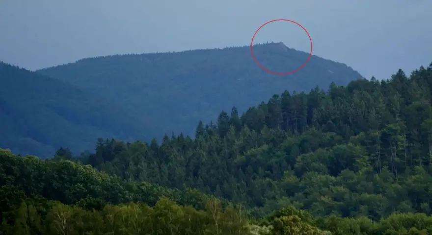 Górzyste krajobrazy czeskich Izery, z zalesionymi zboczami i skalistym szczytem zaznaczonym czerwoną obwódką.