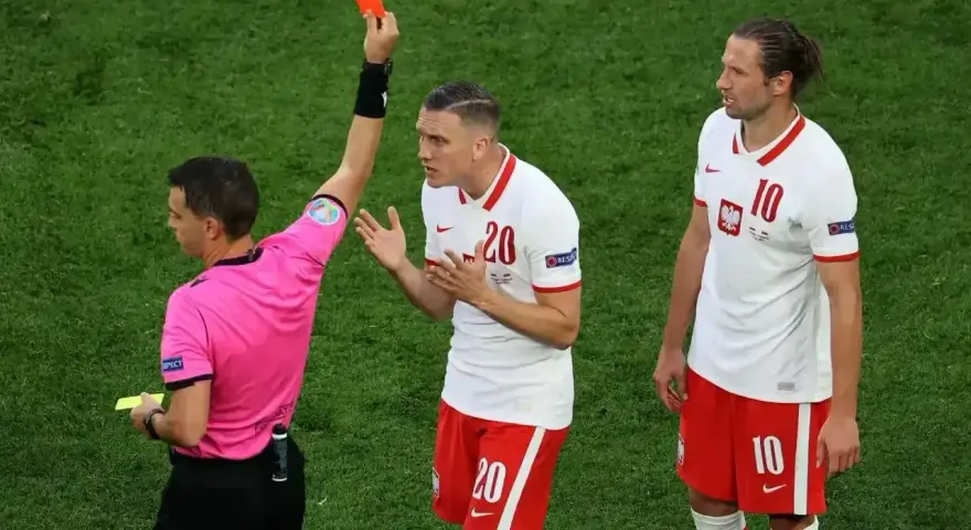 Sędzia pokazuje czerwoną kartkę w siatkówce. Piłkarz z numerem 20 protestuje, obok stoi kolega z numerem 10.
