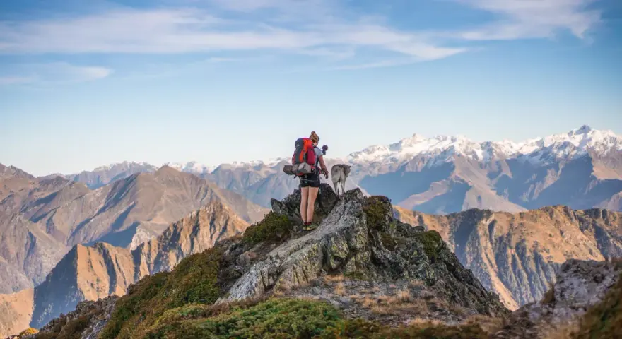 Escursionista con cane su cresta rocciosa, sfondo di montagne innevate nei GR10 Pirenei.