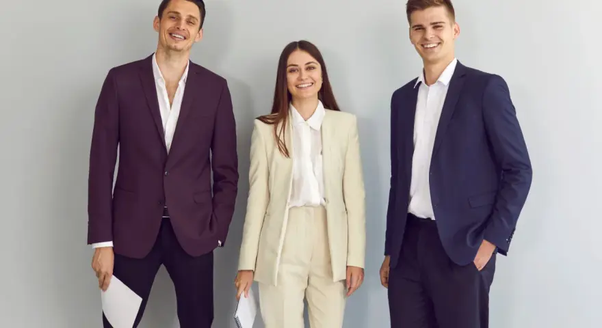 Trzy uśmiechnięte osoby w eleganckich strojach, idealnych na rozmowę o pracę. Dowiedz się, jak się ubrać na rozmowę o pracę!