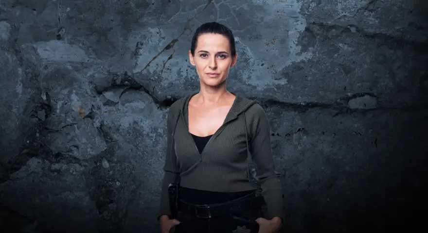 Natalia Brudniak w wojskowym stylu, z rękami w kieszeniach, na tle zniszczonej ściany.