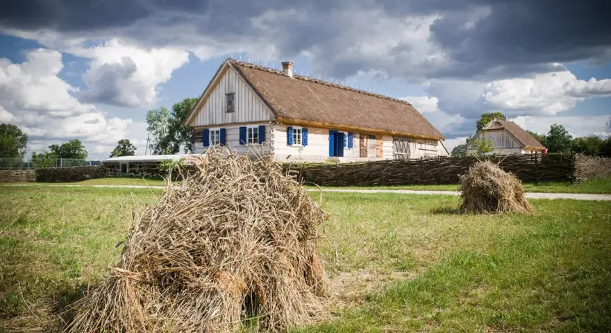 Tradycyjne chaty z krytymi strzechą dachami, jak te w skansenach w Polsce, otoczone plecionymi płotami i stogami siana.