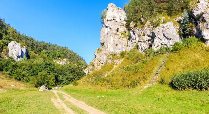 Wspinacze na skalnej ścianie w malowniczym parku krajobrazowym Dolinki Krakowskie. Kręta ścieżka prowadzi przez zielone wzgórza.