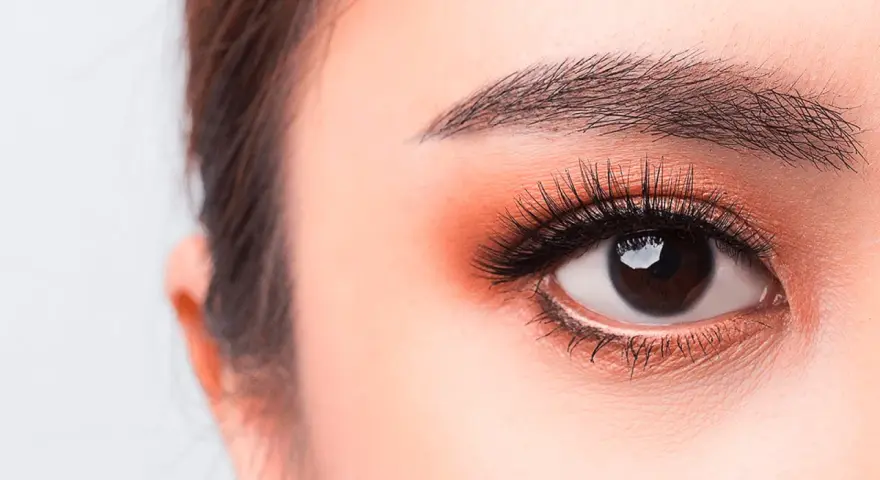 Occhi luminosi con un tocco di trucco coreano: ombretto pesca, eyeliner sottile e ciglia lunghe e folte.