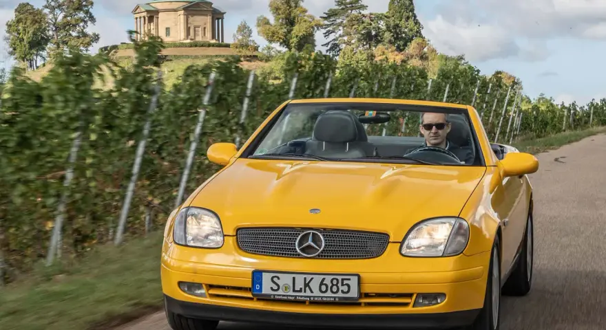 Gelber Mercedes SLK R170 Cabrio fährt durch Weinberge, im Hintergrund ein Tempel.