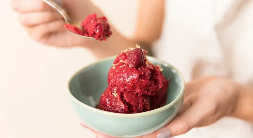 Ein Löffel Himbeersorbet-Rezept wird über eine Schüssel mit dem leuchtend roten Dessert gehalten, garniert mit einer Himbeere.