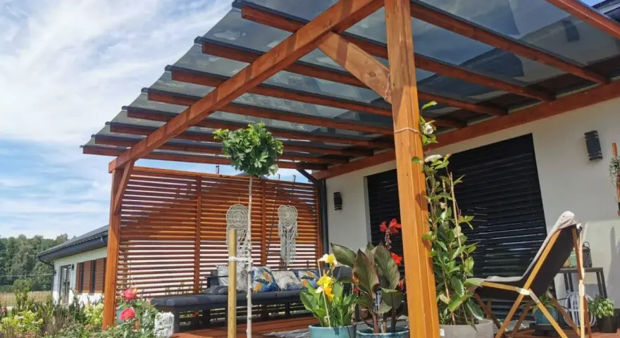 Drewniana pergola z przezroczystym dachem to idealne rozwiązanie co na dach tarasu. Wygodny wypoczynek wśród roślin i kwiatów.