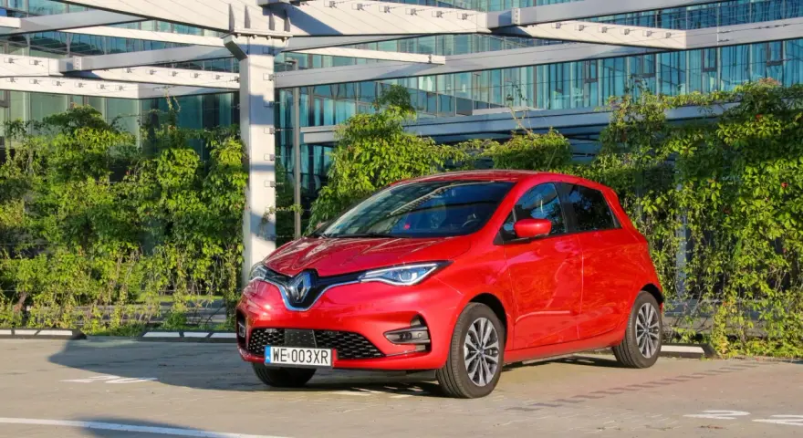 Czerwony Renault Zoe, elektryczny samochód miejski, gotowy do jazdy. Jego imponujący zasięg pozwala na swobodne podróżowanie po mieście i poza nim.