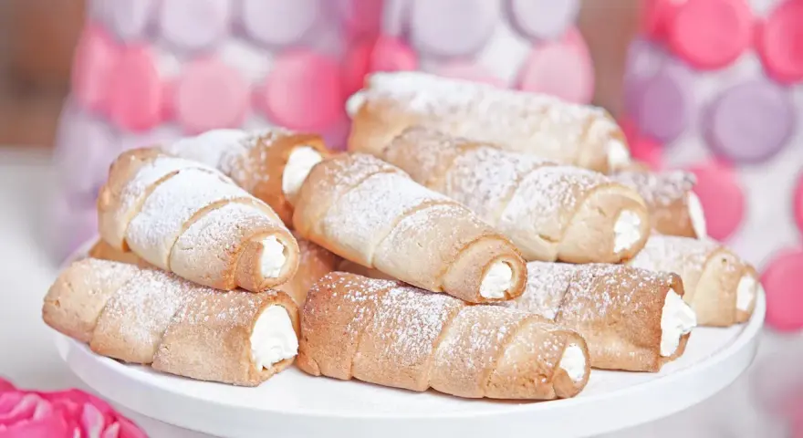 Domowe rurki z kremem, posypane cukrem pudrem, wyglądają apetycznie obok pastelowych dekoracji.
