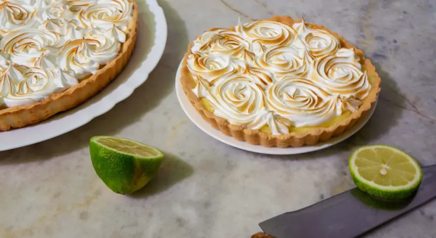 Dos deliciosas tartas de limón con merengue tostado, listas para ser cortadas.