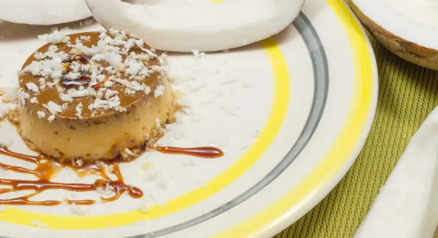 Flan coco on a plate, garnished with coconut flakes and caramel. A perfect dessert for your recette flan coco lait concentré Nestlé.