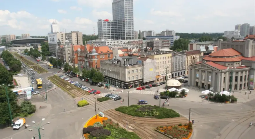 Widok na ruchliwy rynek w Katowicach z tramwajami, samochodami i budynkami.