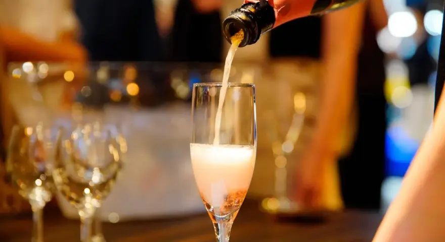 Nalewanie musującego **cava wino** do kieliszka. W tle widać inne kieliszki i rozmyte światła, sugerujące uroczystą atmosferę.