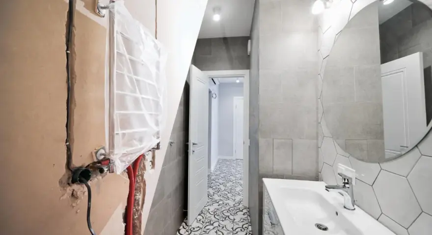 Bagno in ristrutturazione con impianto idraulico a vista, pronto per la detrazione 65. Pavimento decorato e lavabo moderno.