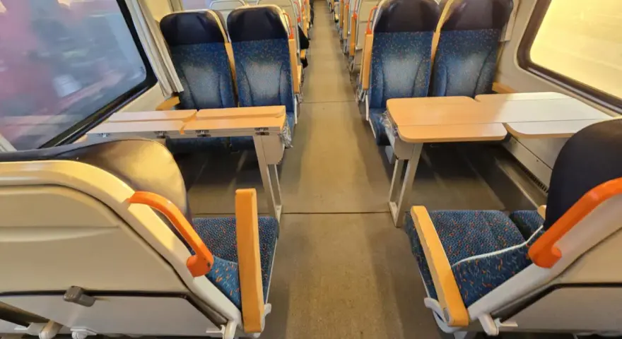 Pociąg do Pragi. Puste siedzenia z niebieskimi obiciami i stolikami czekają na pasażerów.