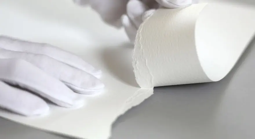 Manos enguantadas manipulan papel texturizado, mostrando su grosor. Esto ayuda a entender qué es el gramaje.