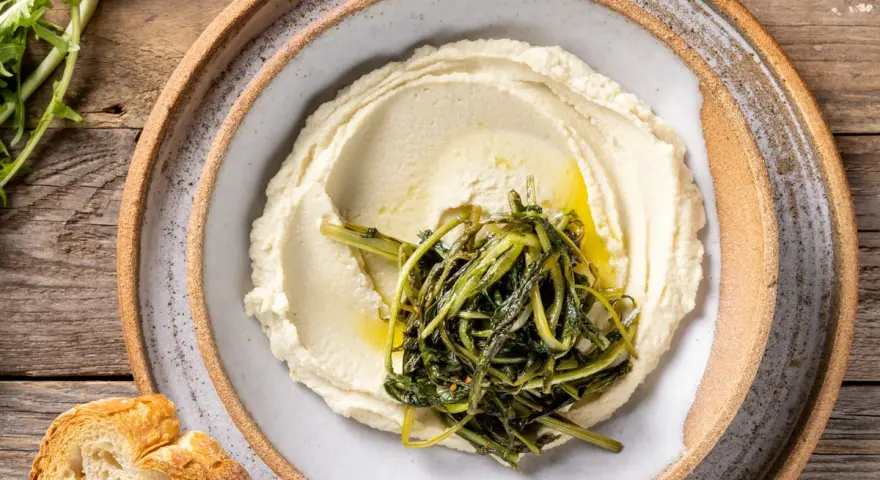 Crema di fave e cicoria saltata, servita su un piatto rustico con pane croccante.