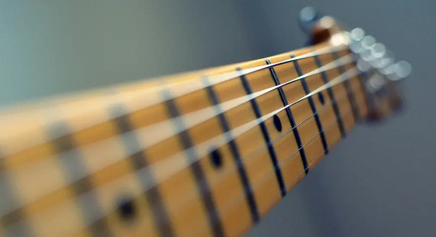 Zbliżenie na gryf gitary, gdzie ja gram na gitarze chwyty. Widać struny i progi.