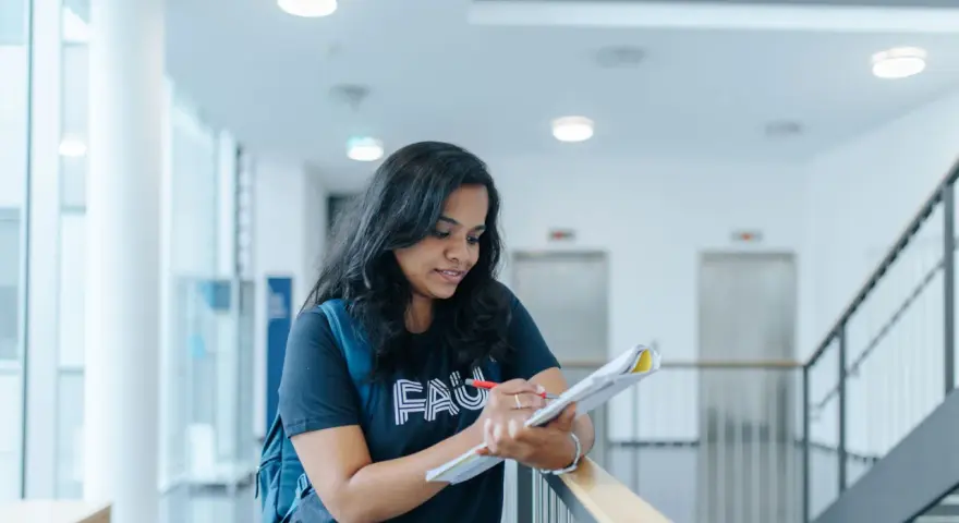 Junge Frau mit Rucksack lernt für die Hochschulreife in einem modernen Gebäude.
