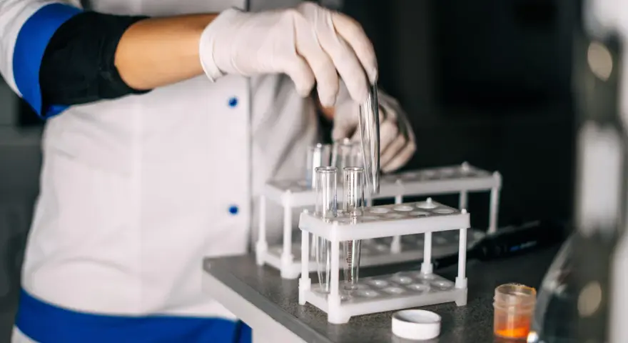 Laborant med handskar hanterar provrör. Kanske för att ta testosteron eller analysera andra prover i labbet.