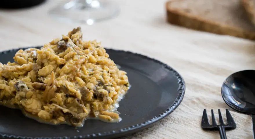 Delicioso revuelto de setas servido en plato oscuro, acompañado de pan y cubiertos.