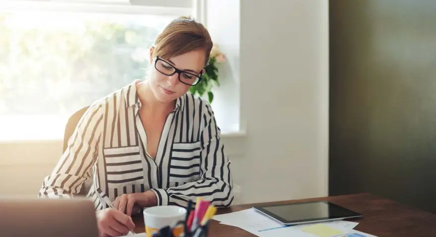 Mujer con gafas trabaja en su escritorio, revisando documentos y gráficos. Quizás está lidiando con gastos de difícil justificación.