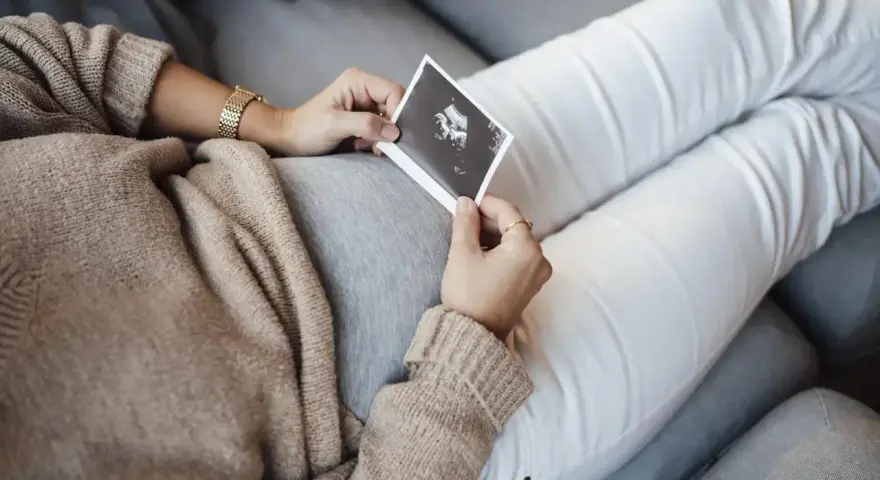Kobieta trzyma zdjęcie USG, na którym widać dziecko. To już 10 tydzień ciąży, a maluch rośnie.