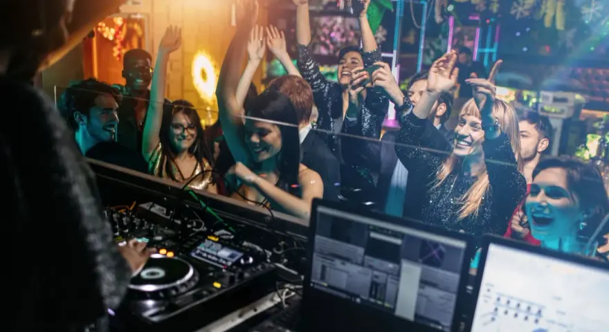 Feiernde Menschen tanzen im Club, während ein DJ auflegt. Eine druckbare muttizettel vorlage zum ausdrucken wäre hier perfekt für die nächste Party!