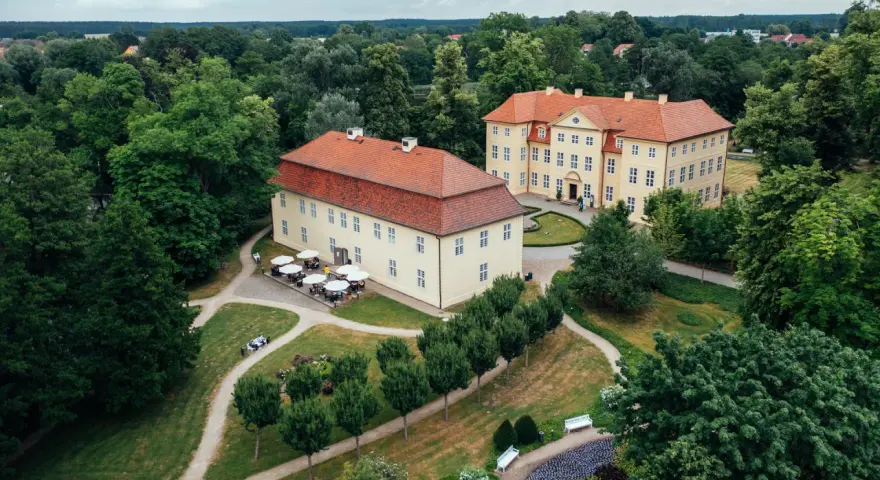 Zwei gelbe Barockschlösser mit roten Dächern auf der Schlossinsel Mirow, umgeben von üppigem Grün und gepflegten Wegen.