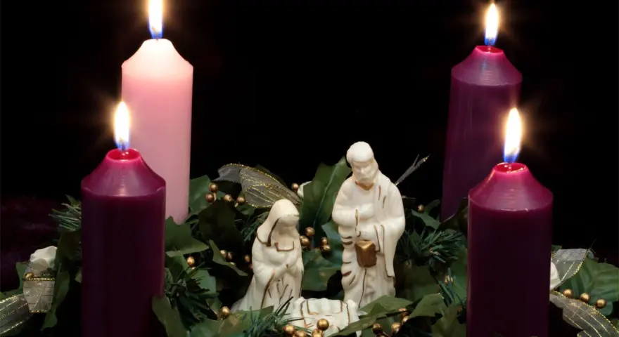 Three lit candles, two purple and one pink, surround a nativity scene. This is the advent 3rd Sunday.