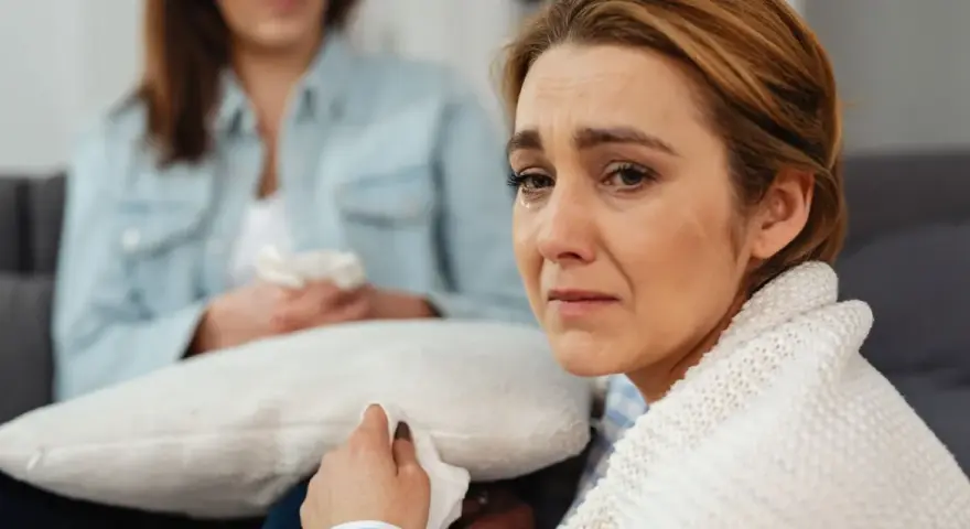 Kobieta płacze, druga osoba podaje jej chusteczkę.