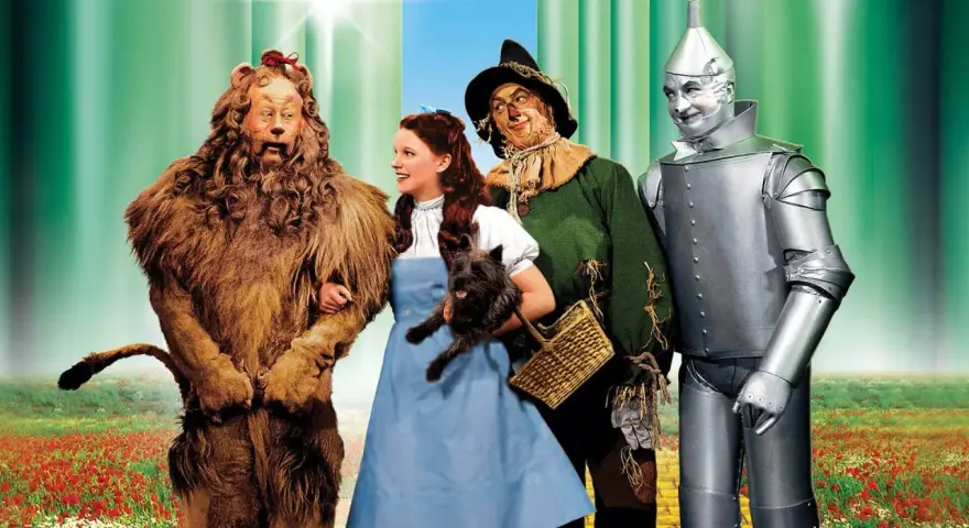 Il leone codardo, Dorothy con Toto, lo spaventapasseri e l'uomo di latta camminano sul sentiero di mattoni gialli. Il linguaggio dei colori evoca un mondo magico.