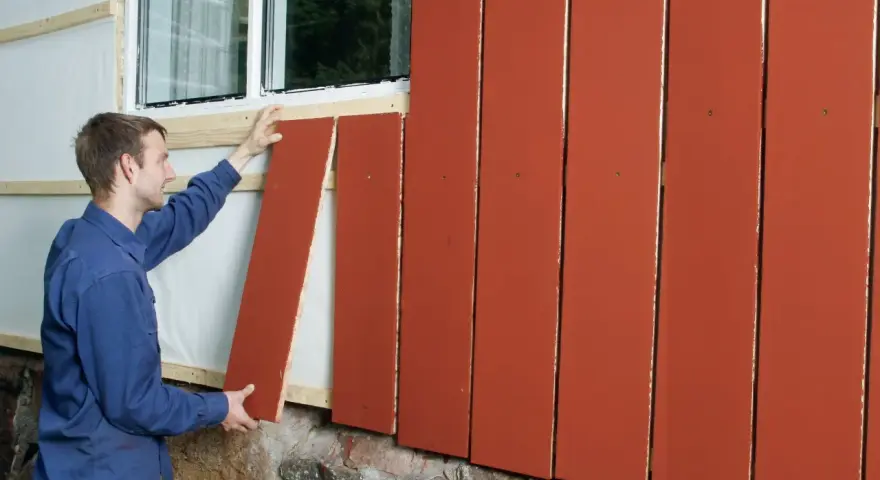 Man monterar en röd lockpanel vid ett fönster.
