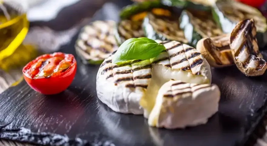 Pyszny camembert z grilla, z rumianymi paskami, podany z grillowanymi warzywami i pomidorkiem.