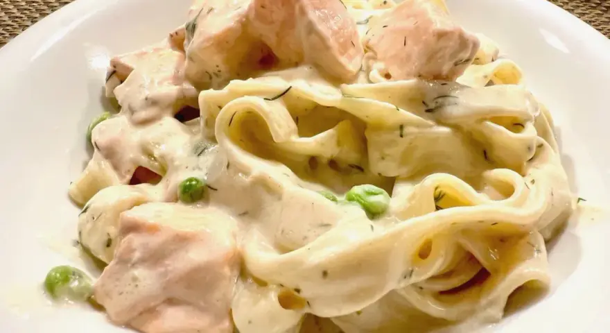 Cremige Nudeln mit Lachs, Erbsen und Dill in einer weißen Schüssel.